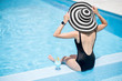 © rh2010 - Young woman in black swimsuit and sun hat sitting back with cocktail in the swimming pool outdoors