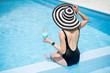 © rh2010 - Young woman in black swimsuit and sun hat sitting back with cocktail in the swimming pool outdoors