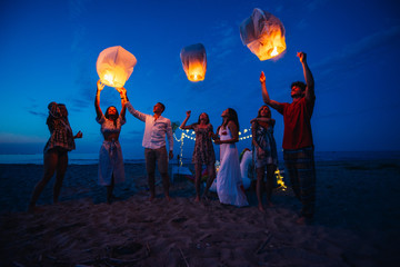 Group of friends making party on the beach at sunset time