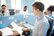 © pressmaster - Serious young businessman with paper sitting by individual workplace among his colleagues