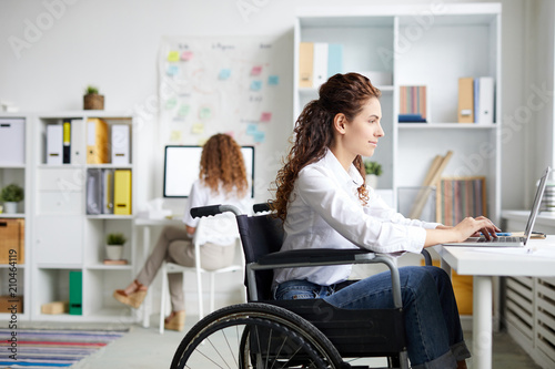 Young Disable Office Worker In Wheelchair Sitting By Desk In Front