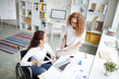 © pressmaster - Two young businesswomen discussing papers or planning work at meeting in office
