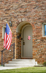 Wall Mural - Entrance to brick house with an arched door flying an American Flag reflected in door window