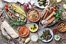 Middle Eastern, Arabic Or Mediterranean Dinner Table With Grilled Lamb Kebab, Chicken Skewers  With Roasted Vegetables And Appetizers Variety Serving On Wooden Outdoor Table. Overhead View.