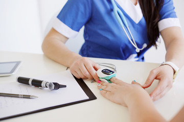 Female doctor with otoscope and pulse oximeter in blue uniform making oxygen test to a patient. Medicine and health care concept.