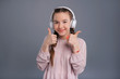 © Viacheslav Yakobchuk - Great song. Adorable teenage girl listening to music in big headphones and showing thumbs up while posing isolated on a blue-grey background