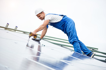 Construction worker connects photo voltaic panel to solar system using screwdriver. Professional installing and construction of solar system, alternative energy and financial investment concept.