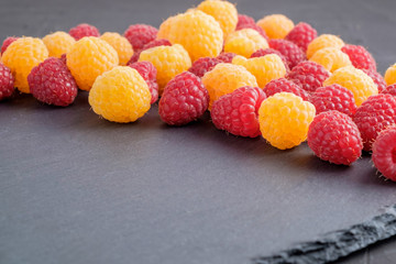 Red and yellow ripe natural raspberries on black stone background. Close-up view. Copy space for text