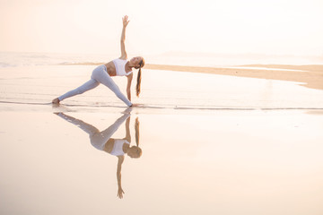 Caucasian woman practicing yoga at seashore of tropic ocean