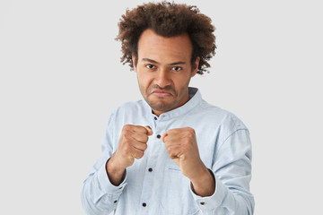 Wall Mural - Attractive African American male ready to struggle, defenses girlfriend, keeps hands in fists, has annoyed expression, dark skin, isolated over white background. Don`t bother me, I will revenge