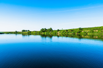 Wall Mural - Bright summer nature panorama, forest trees and river with reflection in water, vivid tranquil and relax background