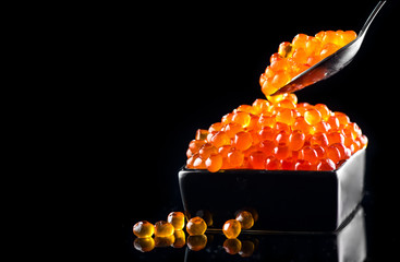 Caviar in a spoon. Salmon caviar in a bowl over black background. Closeup trout caviar