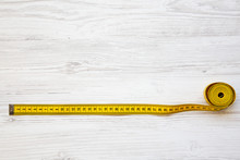 Yellow Measuring Tape On White Wooden Background, Top View. From Above. Copy Space.