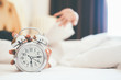 © MIND AND I - Irritated young woman putting her alarm clock off in the morning with soft morning light. Relaxing concept.