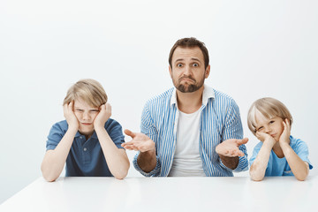 why sons are mad. portrait of clueless nervous father-in-law sitting with two cute boys at table, sh