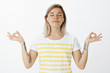 © Cookie Studio - Yoga, lifestyle and youth concept. Portrait of relaxed joyful attractive woman in wireless headphones, standing with spread in both ways hands in zen gesture, smiling and closing eyes, meditating
