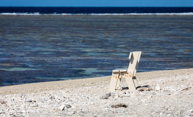 Wall Mural - White wooden bench on a white sand beach in front of a coral lagoon