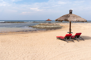 Sun umbrella and two red recumbent places to relax on the beach of Nusa Dua