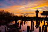 Fototapeta Sypialnia - A silhouette young girl standing with water reflection on twilight of sunset colorful shade