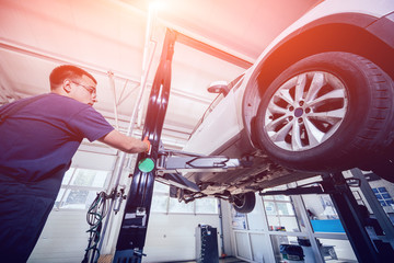 Wall Mural - Car mechanic inspecting wheel and suspension detail of lifted automobile at repair service station