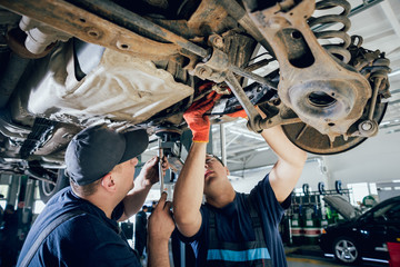 Wall Mural - Car mechanics repair car suspension of lifted automobile at repair service station