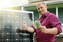 Solar Panel. Money In The Hands Of Men . Energy Production Technologies. Wooden House Background. Saving.