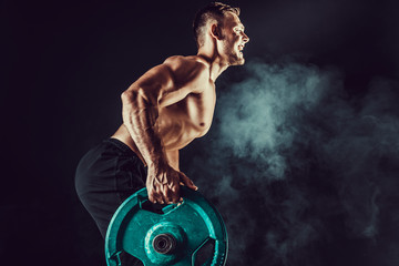 Strong athletic man pumping up muscles workout bodybuilding. muscular bodybuilder handsome men doing exercise for muscles of back with a barbell on dark background with smoke. Strength and motivation.