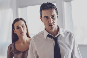 Being depressed. Sad young man looking at you while being angry with his wife