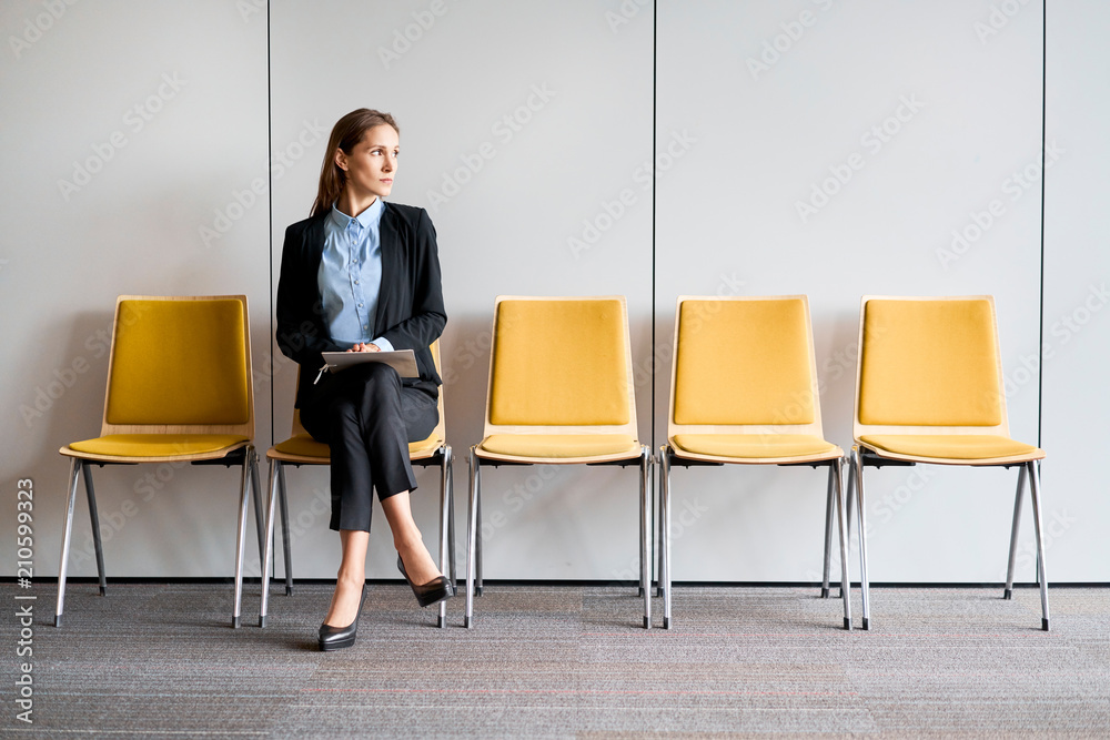 Young woman sitting in lobby with resume in hands and waiting for job interview - obrazy, fototapety, plakaty 