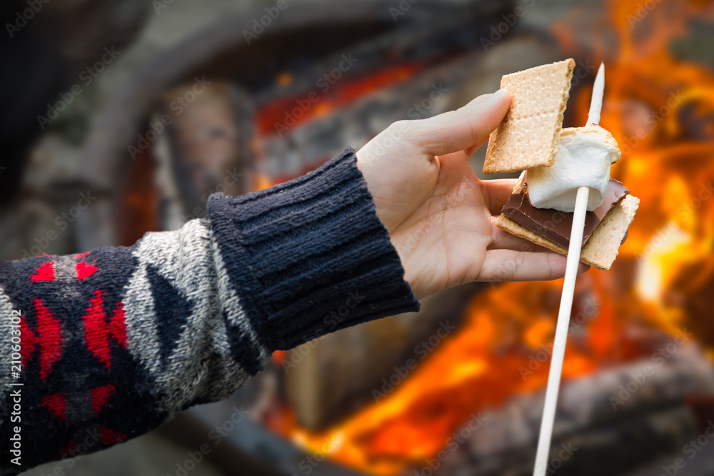 Closeup of Hands Building Smore with Roasted Marshmallow and Chocolate At Campfire Outdoors - obrazy, fototapety, plakaty 