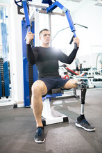 Full Length Portrait Of Handsome Muscular Man With Prosthetic Leg Working Out Using Machines In Modern Gym, Copy Space