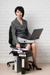 © soleg - business woman with laptop and folders, dressed in a gray suit poses in front of a white wall