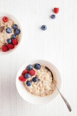 Wall Mural - A bowl of oatmeal porridge with blueberries and raspberries on white wooden table. Top view.