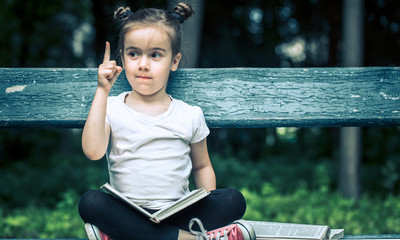 Poster - little girl is sitting on a bench and is reading a book