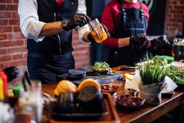 Chef adding souse to other ingridients while making beef burgers indoor at restaurant kitchen