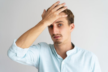 Closeup of tired disappointed blonde guy with face palm gesture. Young Caucasian handsome man covering forehead with hand, suffering from headache. Facepalm or head ache concept