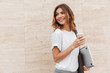 © Drobot Dean - Image of joyful european woman walking against beige wall outdoor with silver laptop, and takeaway coffee in hands