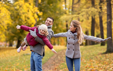 Poster - family, season and people concept - happy mother, father and little daughter playing at autumn park