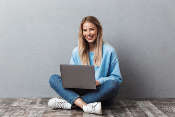 Smiling young blonde girl using laptop computer
