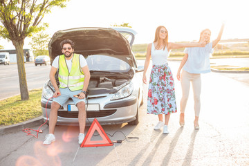 Group of friends stranded on the parking lot by a broken car during road trip. Two women trying to get some help