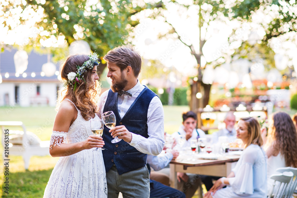 Bride and groom clinking glasses at wedding reception outside in the backyard. - obrazy, fototapety, plakaty 
