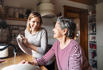 Wall Mural - An elderly grandmother with an adult granddaughter at home, washing the dishes.