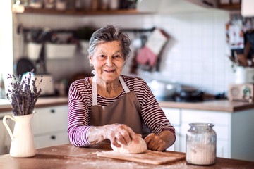 Wall Mural - A senior woman kneading dough in the kitchen at home.