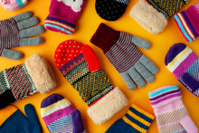 Warm Clothes In The Form Of Mittens And Gloves. Colorful Mittens And Gloves Scattered On A Yellow Background. View From Above.