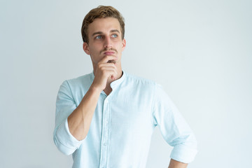 Wall Mural - Pensive young man touching chin and looking away. Handsome guy thinking. Contemplation concept. Isolated front view on white background.