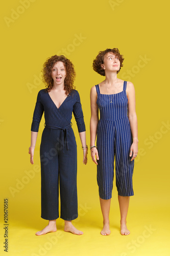 Indoor Shot Of Two Caucasian Females In Similar Blue Overalls