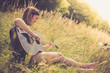 Junges Mädchen sitzt in der Wiese und spielt Gitarre