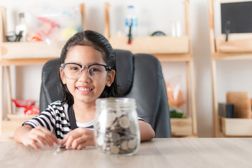 Wall Mural - Asian little girl in smiling with the coin in a glass jar for saving money concept shallow depth of field select focus at the face