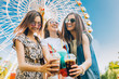 © Aliaksandr Barouski - Summer lifestyle portrait multiracial women enjoy nice day, holding glasses of milkshakes. Happy friends inin front of ferris wheel. Best friends girls having fun, joy. Lifestyle. Asian, jewess and