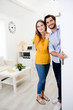© W PRODUCTION - cheerful young couple man and woman welcome friends at open front door new student home apartment